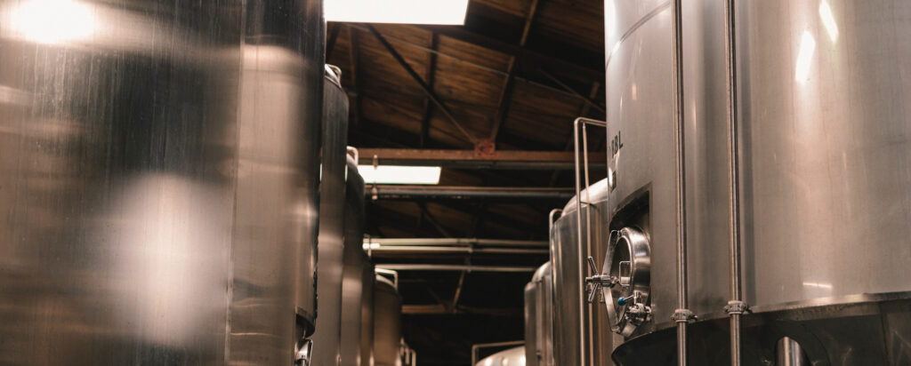 Large stainless steel industrial tanks inside a warehouse with a wooden ceiling.