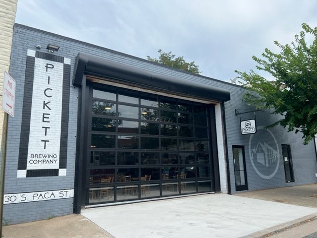 The storefront of Pickett Brewing Company, featuring a large glass garage door, gray brick walls, and a vertical sign reading Pickett Brewing Company.