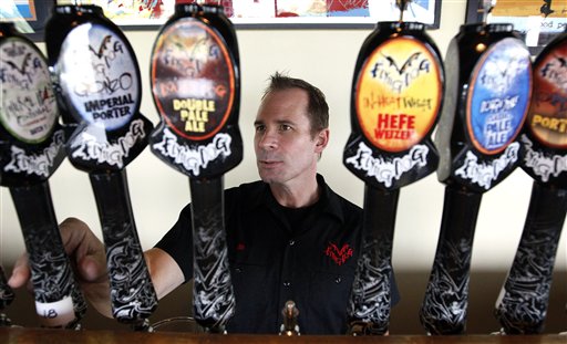 A bartender stands behind a row of Flying Dog beer taps, reaching toward one.