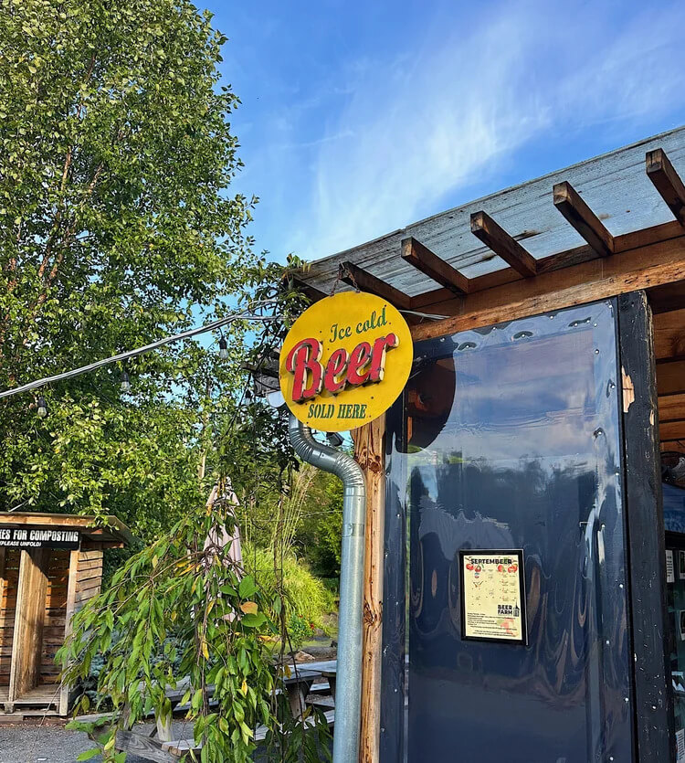 A yellow circular sign reads “Ice cold Beer SOLD HERE” hanging above a structure with a dark plastic door and a September event poster.