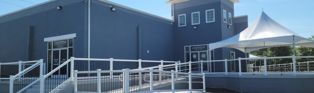 The blue exterior of 5th Company Brewing, featuring a ramp entrance with white railings and a large white canopy tent to the side.