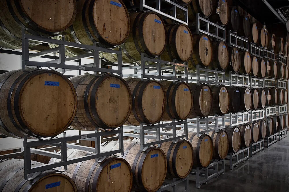 Wooden barrels stacked in metal racks inside a warehouse.