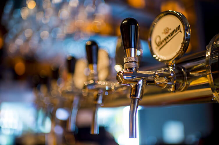 A row of chrome beer taps at a bar, with a Staropramen logo on the front tap.