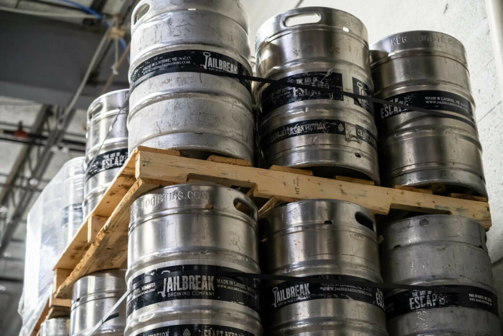 Stacked metal beer kegs from Jailbreak Brewing Company on wooden pallets.