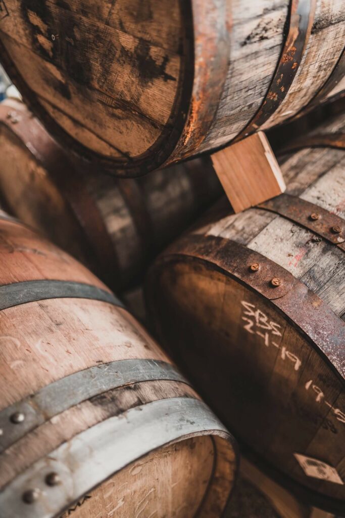 Stacked wooden barrels with rusted metal hoops, one marked with handwritten white text.