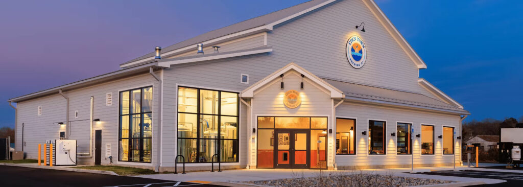 Exterior of Eden Town Brewing Co. at twilight, showing large windows revealing brewing tanks inside and a lit entrance.